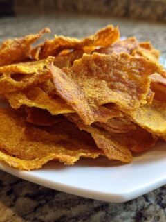 A close-up of a pile of crispy, orange-yellow 2 Ingredient Easy Pizza Chips served on a small white plate.