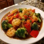 Close-up of Aute Shrimp and Fish Recipe featuring plump shrimp, broccoli florets, and red bell peppers in a savory brown sauce.