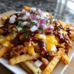 Close-up of BBQ Loaded Chicken Taco Fries topped with melted cheese, BBQ sauce, and diced red onions.