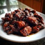 Close-up of glistening, dark glazed pieces of Best Black Pepper Chicken piled high on a white plate.