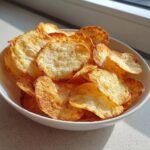A white bowl filled with golden, crispy 2 Ingredient Easy Pizza Chips catching the sunlight.