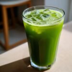 Close-up of a tall glass filled with bright green Celery Pineapple Detox Mocktail and ice cubes.