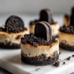 A close-up of one of the Classic Halloween Graveyard Cheesecake Bites, featuring a dark cookie crust, creamy filling, and a cookie 'tombstone'.
