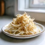 A small white plate piled high with cooked, lightly browned Enoki Mushrooms Benefits.