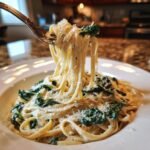 A fork lifting long strands of Creamy Roasted Garlic Kale Pasta With Parmesan from a white bowl.