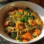 A close-up of Date Night Healthy Shrimp Lo Mein featuring plump shrimp, noodles, carrots, and broccoli, topped with green onions.