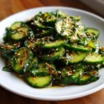 A close-up of sliced cucumbers tossed in a savory dressing, topped with sesame seeds, making an Easy Asian Cucumber Salad.