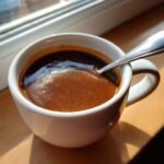Close-up of rich brown Easy Make Ahead Gravy being tested for consistency with a spoon in a white mug.