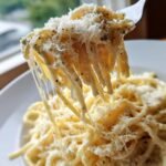 Close-up of spaghetti noodles being lifted by a fork, coated in creamy sauce and topped with grated cheese from an Easy Ricotta Pasta Recipe.