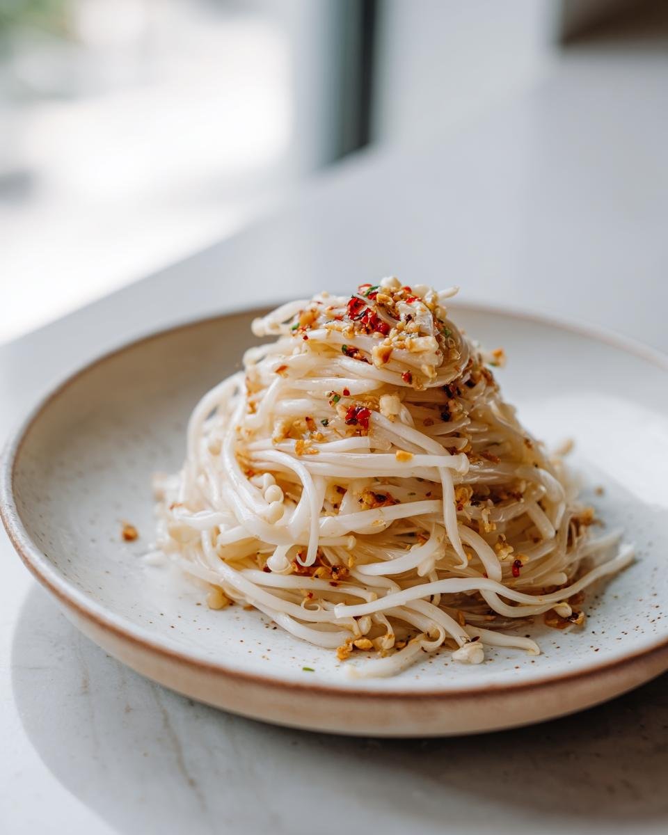 A serving of cooked Enoki Mushrooms Benefits How To Cook, seasoned with chili flakes and garlic, presented on a speckled white plate.