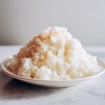 A mound of freshly cooked, fluffy white Coconut Rice served on a small white plate.