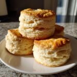 A stack of four golden brown, fluffy Homemade Buttermilk Biscuits resting on a white plate.