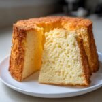 Close-up of a fluffy, golden-brown Lemon Chiffon Cake Recipe with one slice cut out, showing its airy texture.