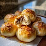 A pile of golden brown Garlic Parmesan Cheeseburger Bombs, one is broken open revealing the seasoned ground beef filling.