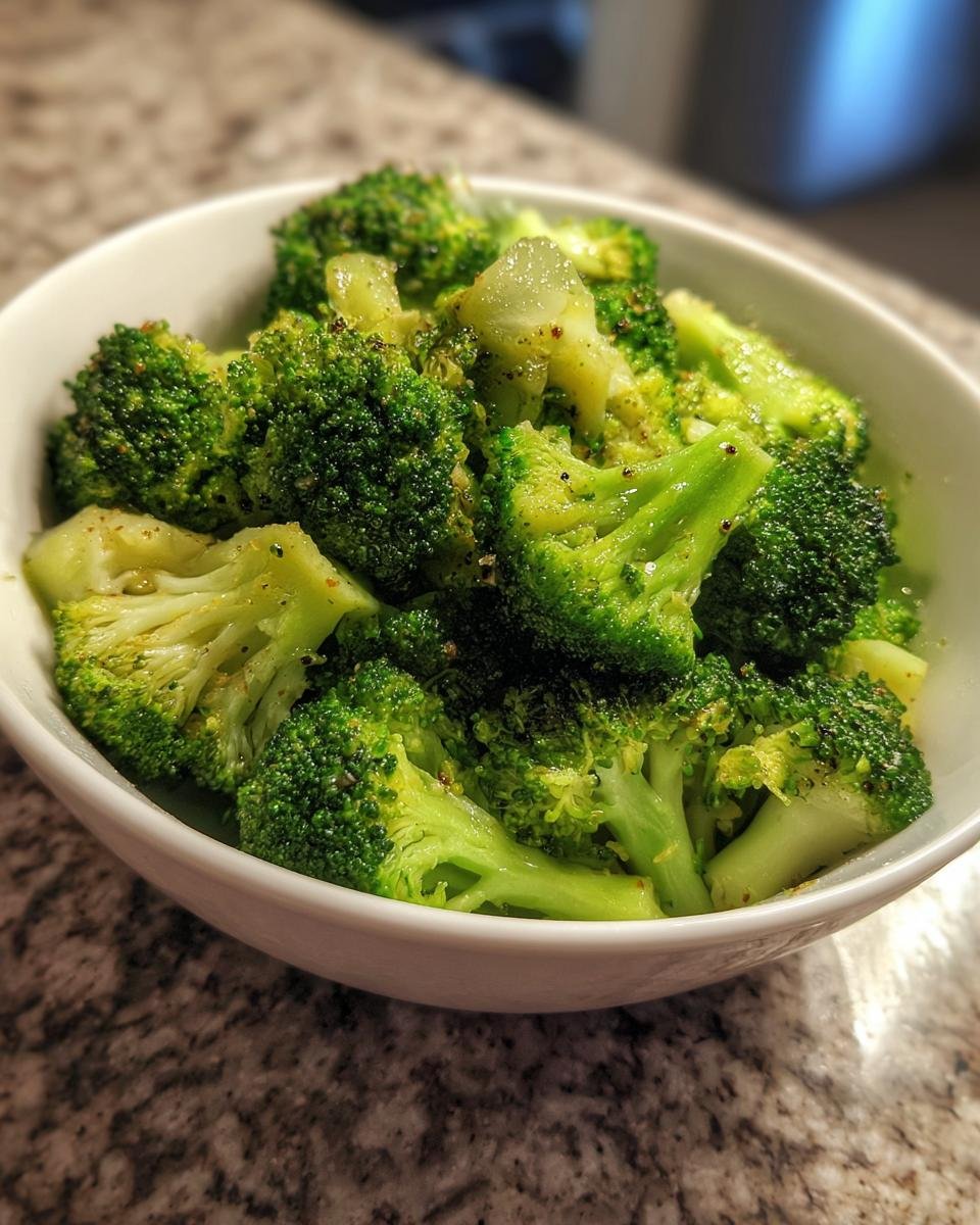 Close-up of bright green Garlic Seasoned Steamed Broccoli florets seasoned with pepper in a white serving bowl.
