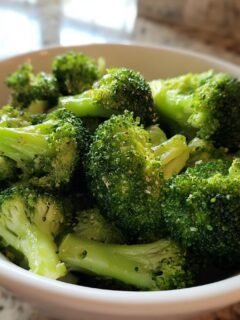 Close-up of vibrant green Garlic Seasoned Steamed Broccoli florets seasoned with visible spices in a white serving bowl.