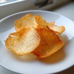 Close-up of several delicate, golden-brown Almond Crisps sprinkled with black pepper on a white plate.