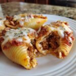 Close-up of baked Ground Beef Stuffed Shells topped with melted mozzarella cheese and herbs on a white plate.