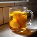 Close-up of steaming Healthy Citrus Pear Ginger Detox Tea with visible pear slices in a clear glass mug.