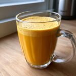 Close-up of a vibrant orange Healthy Pineapple Strawberry Turmeric Smoothie in a clear glass mug.