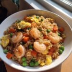 A white bowl filled with Healthy Weeknight Shrimp Fried Rice featuring plump shrimp, peas, diced carrots, and scrambled egg pieces.