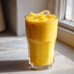 A vibrant, thick Jamaican Pineapple Smoothie topped with frozen pineapple chunks and ice cubes.