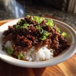 A close-up of a Korean Ground Beef Bowl featuring saucy ground beef over white rice, garnished with green onions and sesame seeds.