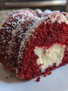 A slice of Layered Red Velvet Cheesecake Bundt Cake showing the vibrant red cake and creamy white cheesecake center, dusted with powdered sugar.