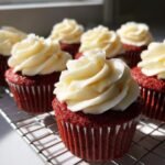 Close-up of a mini red velvet cupcake topped with swirled cream cheese frosting, cooling on a wire rack.