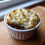 A close-up of a single serving Mini Shepherds Pie with golden, fluffy mashed potato topping in a white ramekin.
