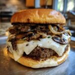 Close-up of a juicy Mushroom Swiss Burger topped with melted Swiss cheese and saut&eacute;ed mushrooms and onions.