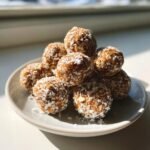 A stack of homemade Energy Balls coated in shredded coconut and oats, brightly lit by sunlight.