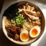 Overhead view of a bowl of Nourishing Homemade Chicken Ramen topped with shredded chicken, soft-boiled eggs, and green onions.