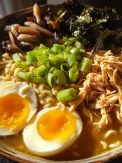 A close-up overhead view of a bowl of Nourishing Homemade Chicken Ramen topped with shredded chicken, soft-boiled eggs, and scallions.