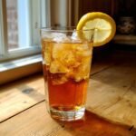 A tall glass filled with ice and amber-colored Orchids Sweet Tea, garnished with a lemon slice.
