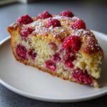 Close-up of a moist slice of Raspberry Almond Cake topped with fresh raspberries and powdered sugar.