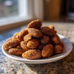 A close-up of a white plate piled high with freshly Roasted Cinnamon Almonds Recipe, coated in sugar and spice.