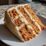 A tall slice of moist Carrot Cake With Maple Cream Cheese Frosting showing three layers of cake and frosting.