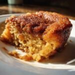 A close-up, sunlit shot of a single, moist slice of Snickerdoodle Cobbler on a white plate.