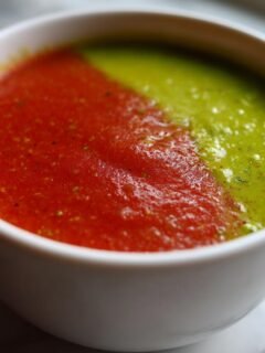Close-up of Spicy Avocado and Tomato Soup served in a white bowl, split between vibrant red tomato and bright green avocado halves.