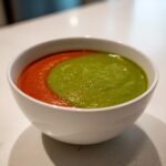 A white bowl containing Spicy Avocado and Tomato Soup, beautifully swirled with vibrant red and green sections.