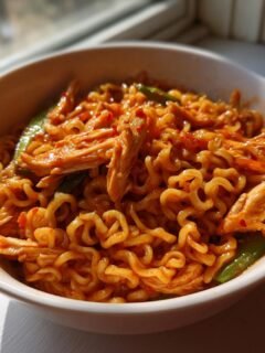 Close-up of a white bowl filled with Spicy Chili Garlic Ramen With Chicken Veggies, coated in a vibrant red sauce.