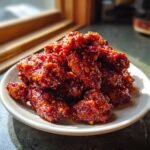 A close-up of a pile of glistening, dark red Spicy Party Wings coated in a thick, sweet and spicy glaze with visible chili flakes.
