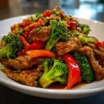 Close-up of a savory stir-fry featuring glazed meat pieces, bright green broccoli, and red bell peppers, part of What To Eat This Week 10 1.
