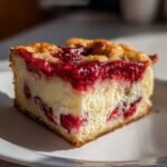 Close-up of a square slice of Strawberry Cheesecake Dump Cake showing creamy filling and bright red berry topping on a white plate.