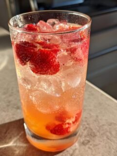 Close-up of a tall glass filled with a bubbly Strawberry Grapefruit Mocktail, ice, and fresh strawberry slices.
