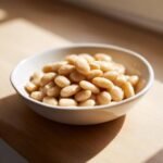 A small white bowl filled with cooked white beans, illuminated by sunlight, relevant to 5 Tips For Better Bean Digestion.