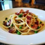 Close-up of creamy Bacon And Pea Pasta tossed with bright green peas and topped with crispy bacon pieces.
