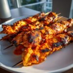 Close-up of several grilled Bang Bang Chicken Skewers coated in a vibrant orange sauce, showing charred grill marks.