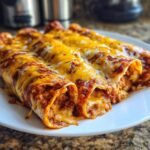 Close-up of three rolled Bean And Cheese Enchiladas smothered in red sauce and melted cheddar and Monterey Jack cheese.